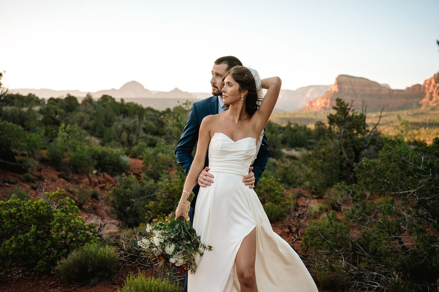 Bride and groom share a romantic moment at sunset in Sedona, Arizona, surrounded by red rocks and desert landscape.