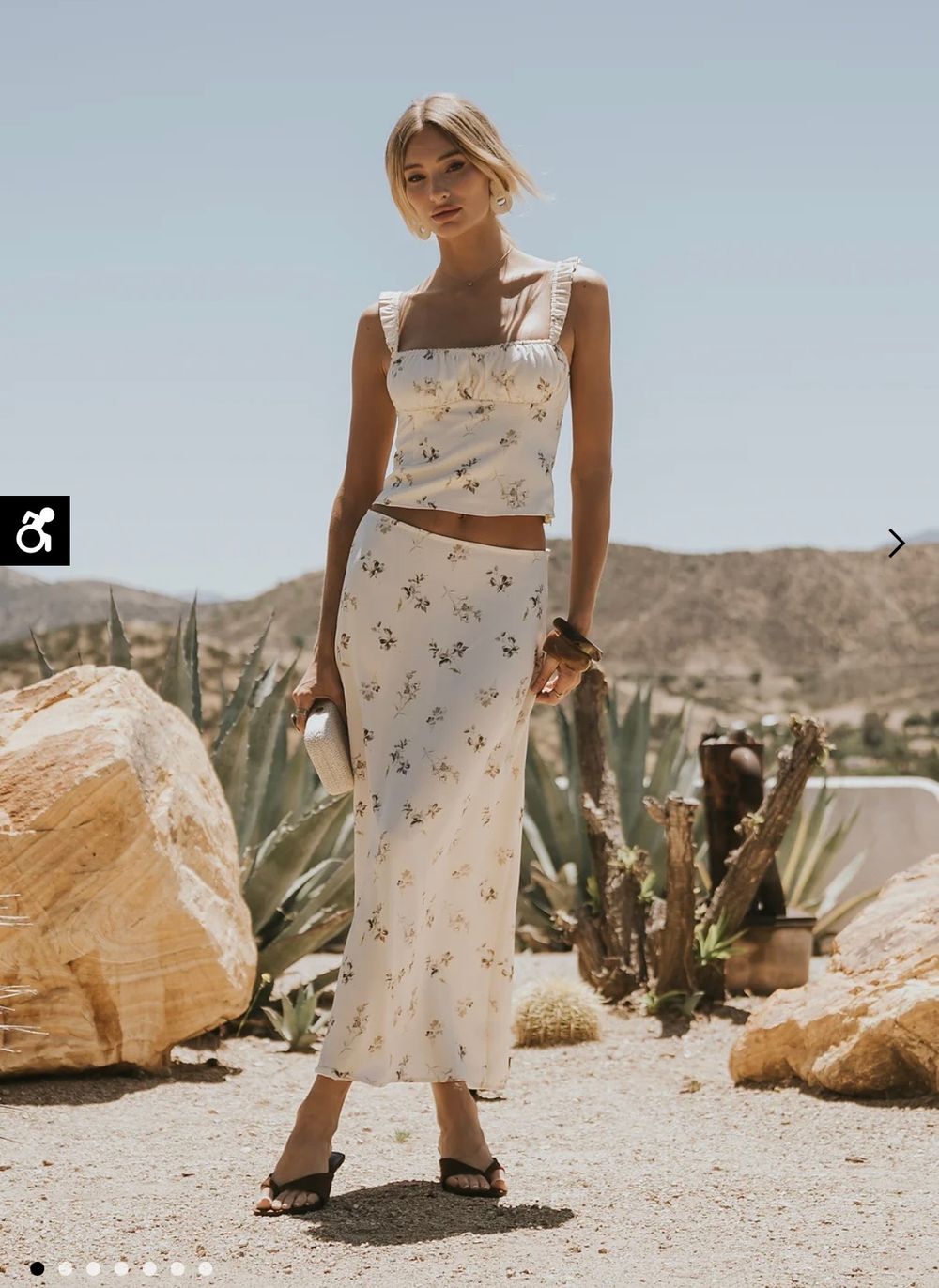Woman wearing a white floral crop top and maxi skirt set in a desert landscape with cacti and boulders.
