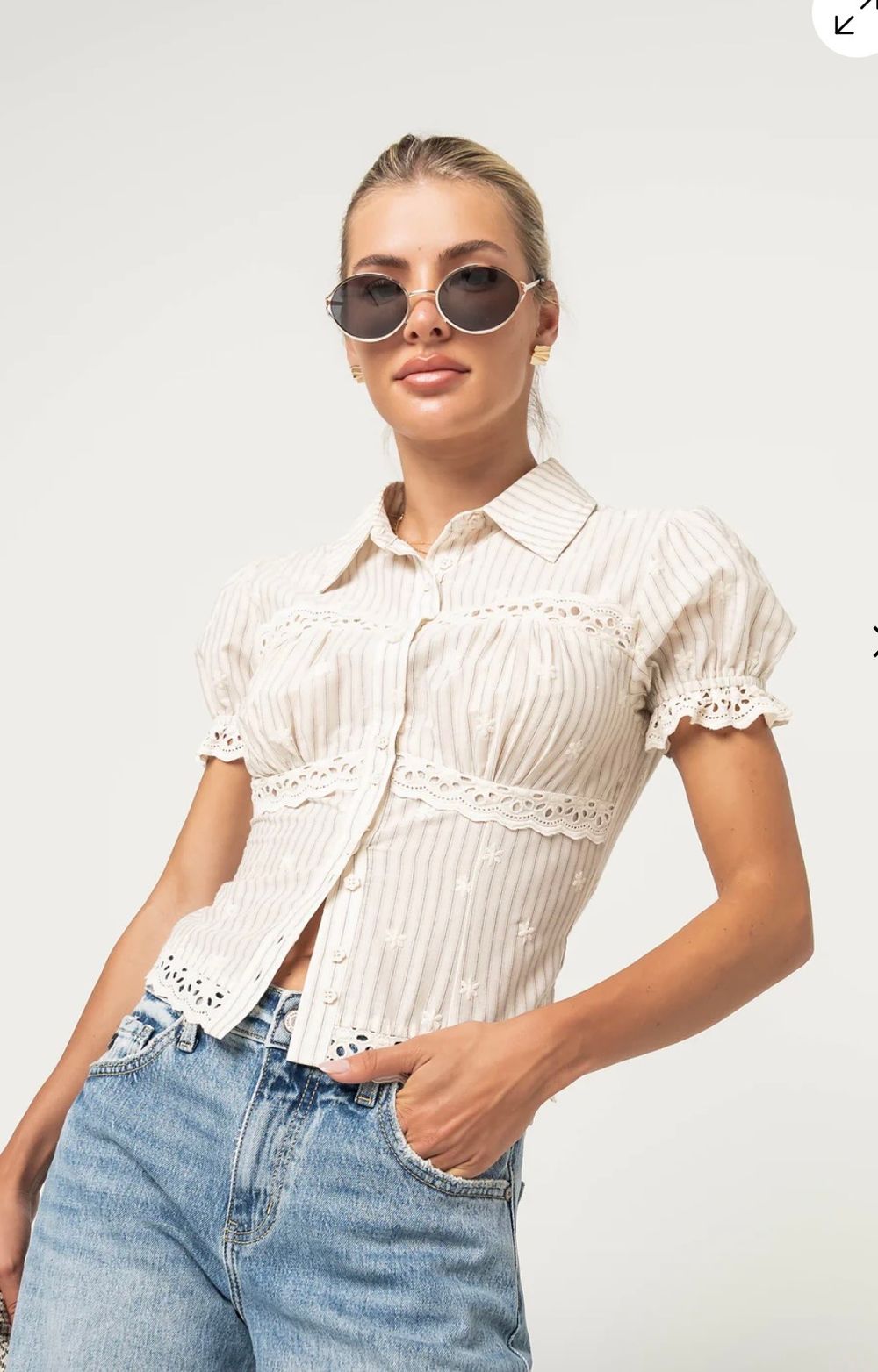 Woman wearing a striped cream eyelet lace crop button-up shirt with puff sleeves, paired with blue jeans.