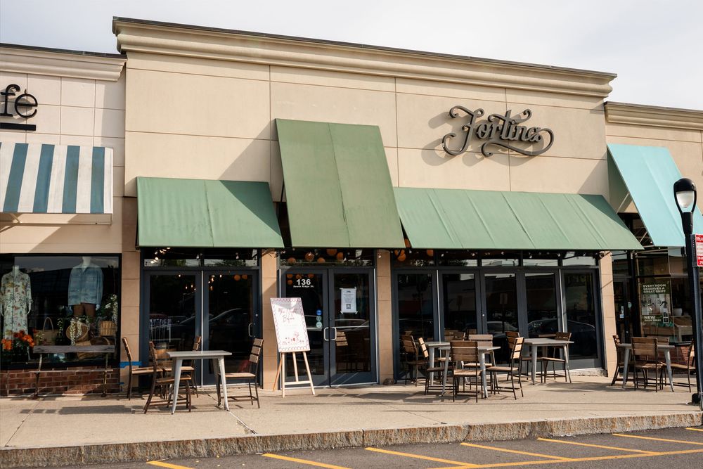 Jardins restaurant exterior with green awnings, outdoor patio seating, and large windows in a strip mall setting.