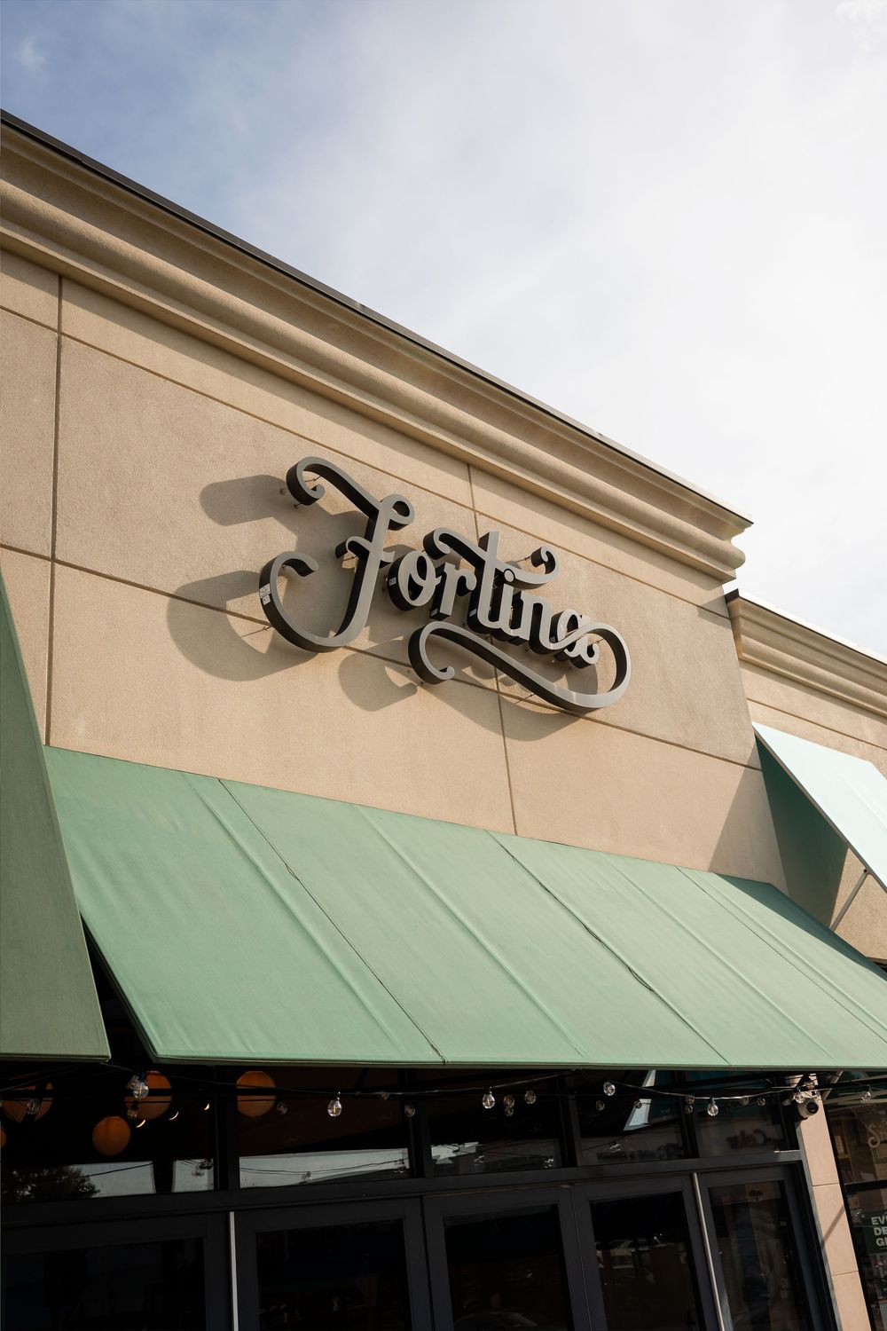 Fortune restaurant storefront with elegant script signage on beige wall above green striped awning.