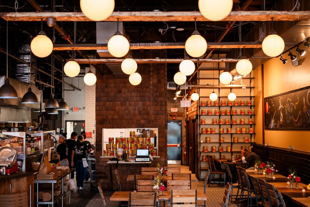 Cozy restaurant interior with globe pendant lights, exposed brick walls, wooden furniture, and open kitchen.
