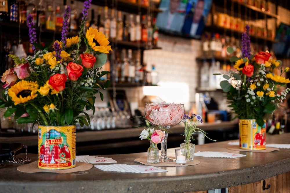 Colorful flower arrangements with sunflowers on a bar counter with bottles in the background.