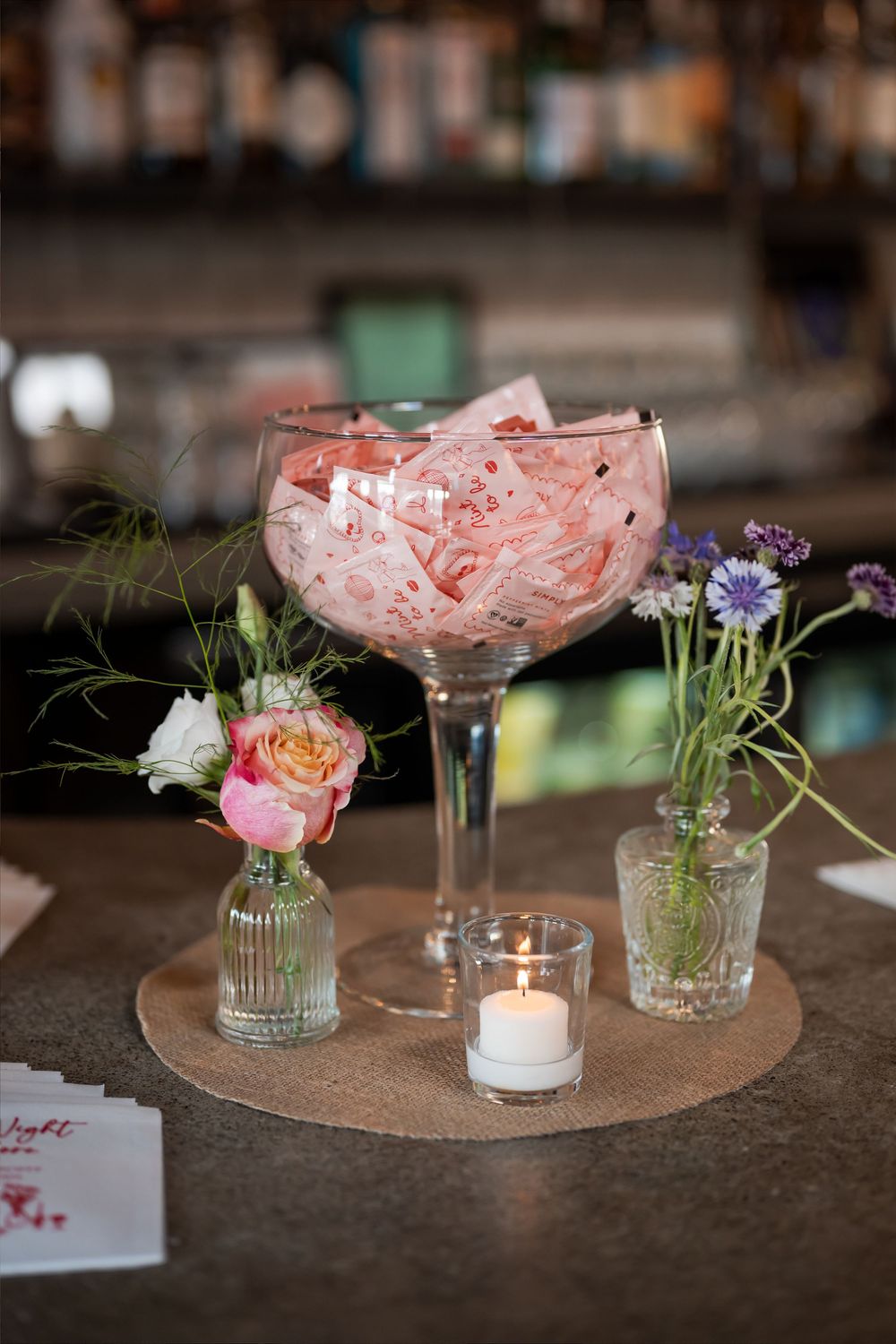 Elegant bar centerpiece with pink roses in a large glass, small floral vases, and a lit tealight candle.