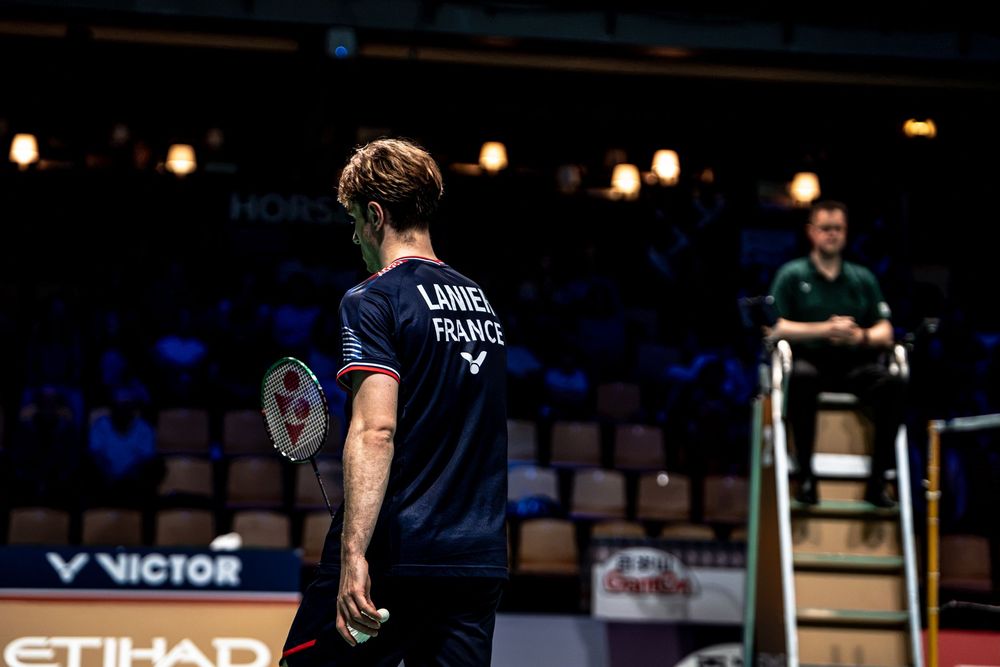 French badminton player LANNEL competes at a VICTOR-sponsored tournament, holding a racket on an indoor court.