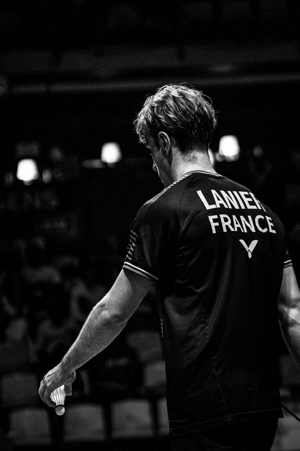 Black and white photo of badminton player Lanier representing France, holding a shuttlecock on a competitive court.