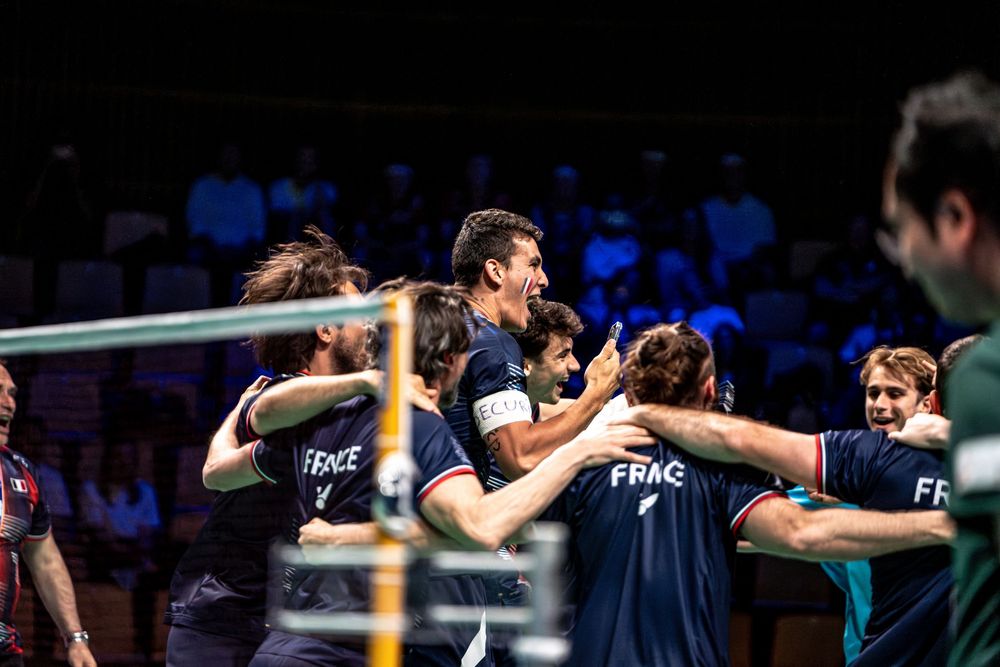 French volleyball team celebrating victory together on court, wearing dark blue France jerseys during a tournament match.