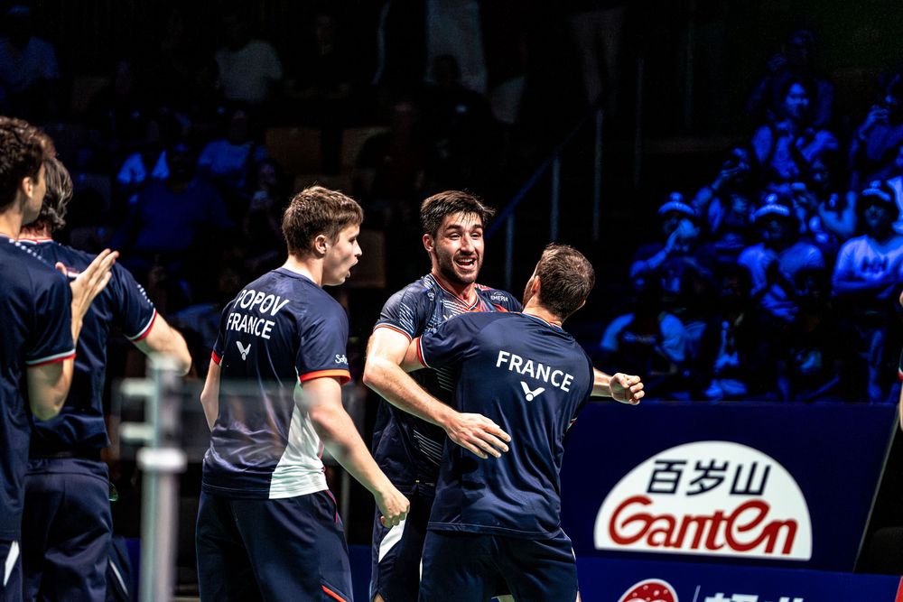 French badminton team players celebrating victory together on court at Ganten tournament.