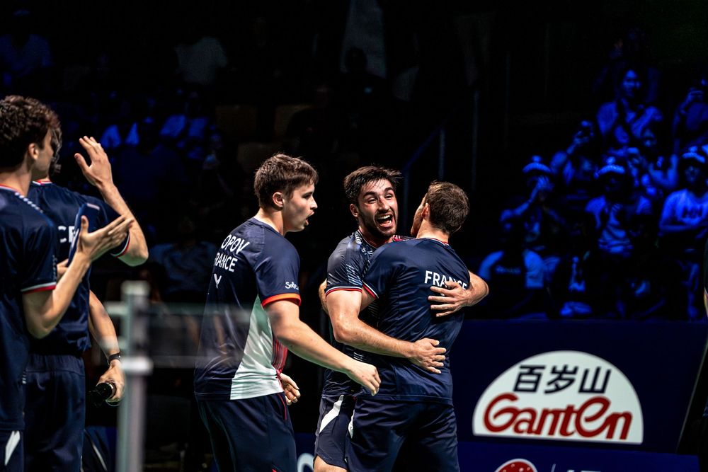 French badminton team players celebrating victory together on court at international championship tournament.