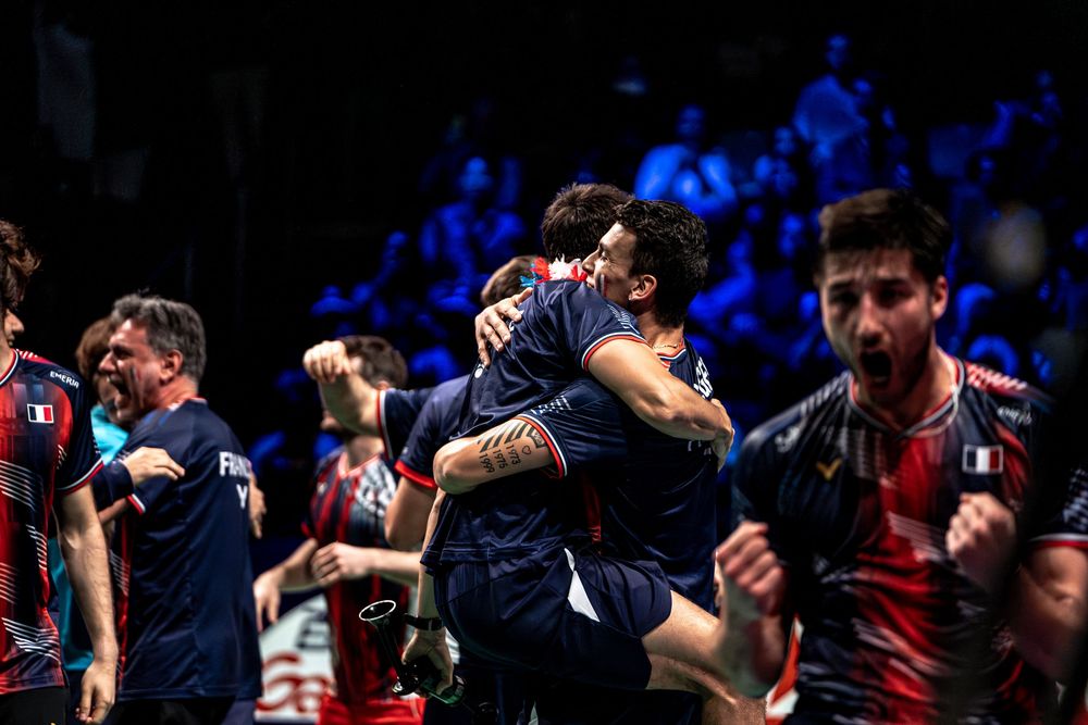 Italian athletes celebrate victory with emotional embraces on a badminton court during a championship match.