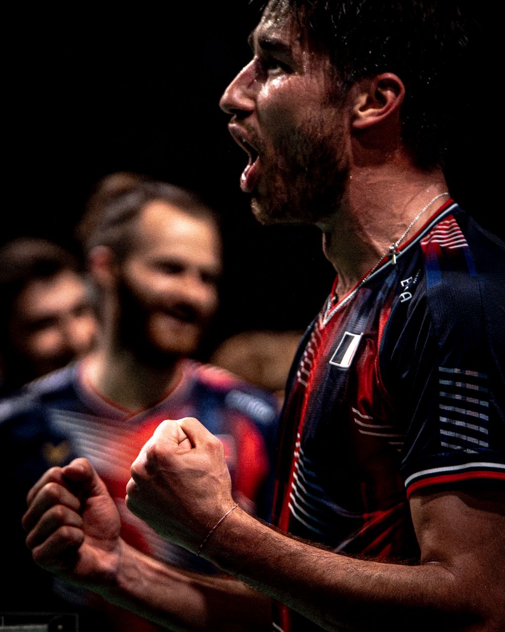 French badminton player celebrating with fist pump, wearing navy France jersey during match.