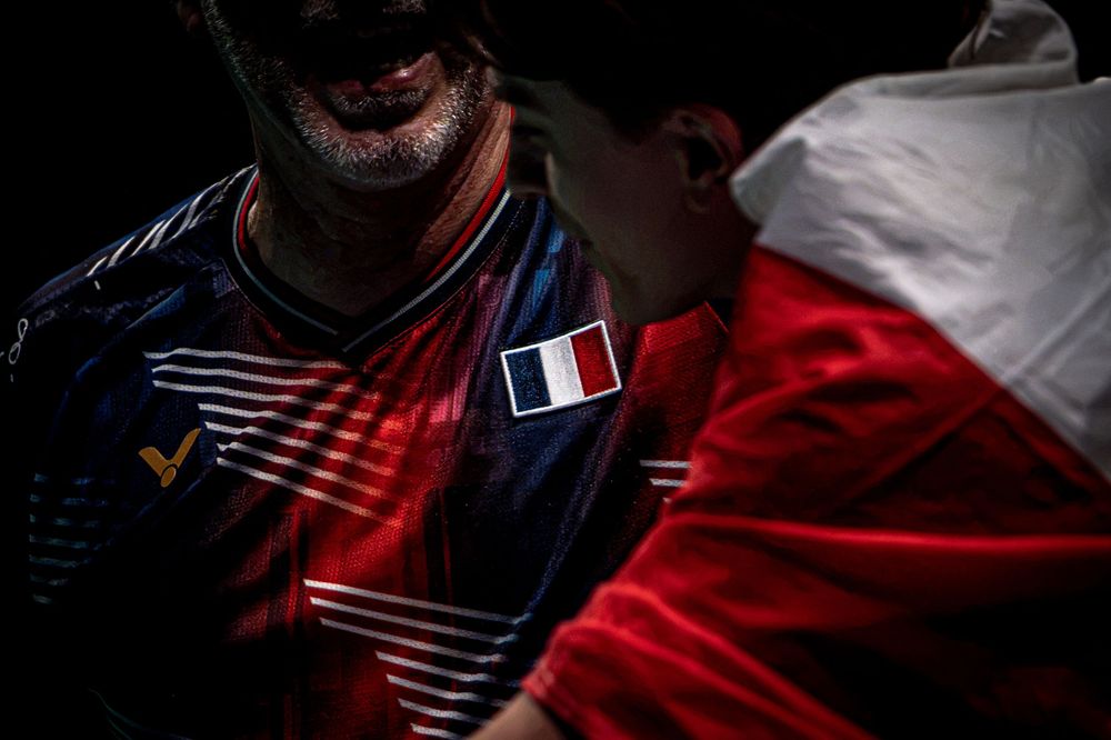 French athlete in navy jersey with French flag patch, dramatically lit against dark background with red and white fabric.