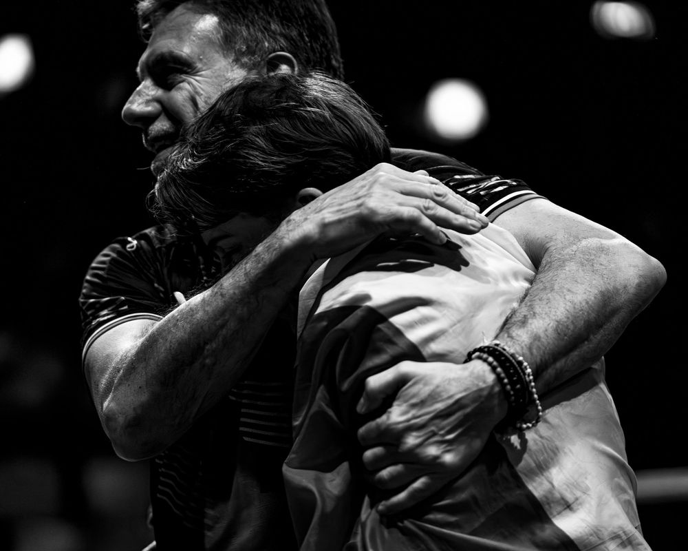 Two athletes share an emotional embrace in athletic wear under dramatic lighting at a sports competition.