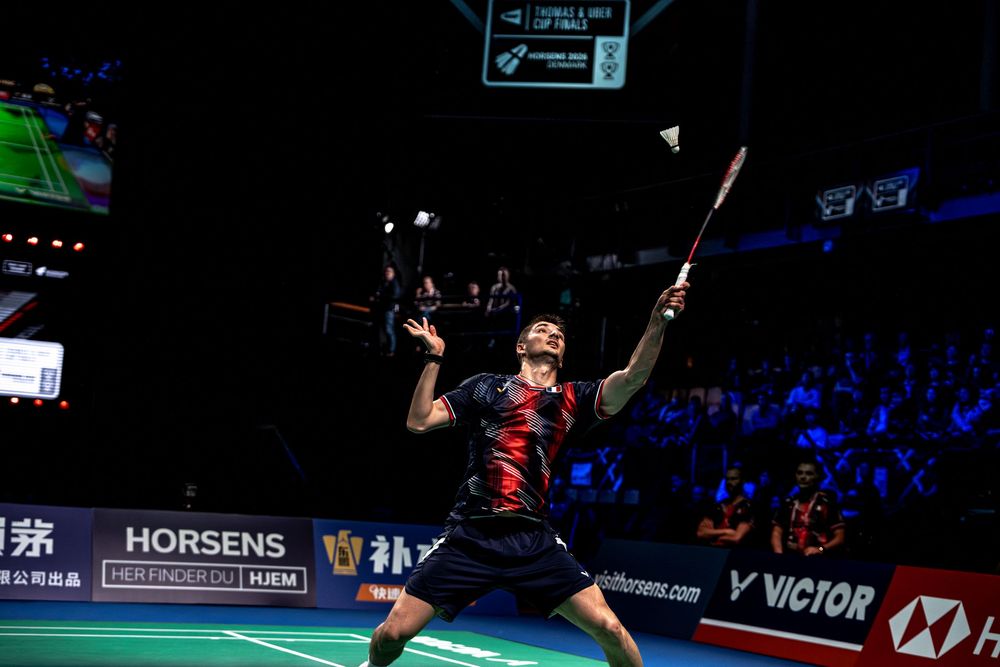 Professional badminton player leaps mid-air executing a powerful smash shot during a Victor tournament match.