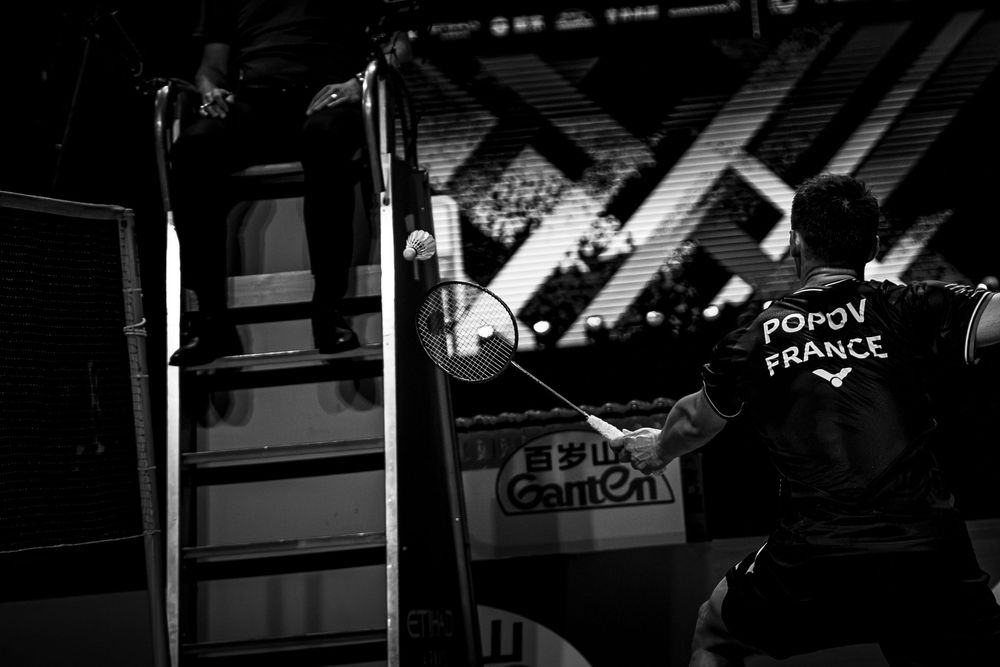 Badminton player mid-match at a professional tournament with HSBC and Etihad Airways sponsorship banners visible.