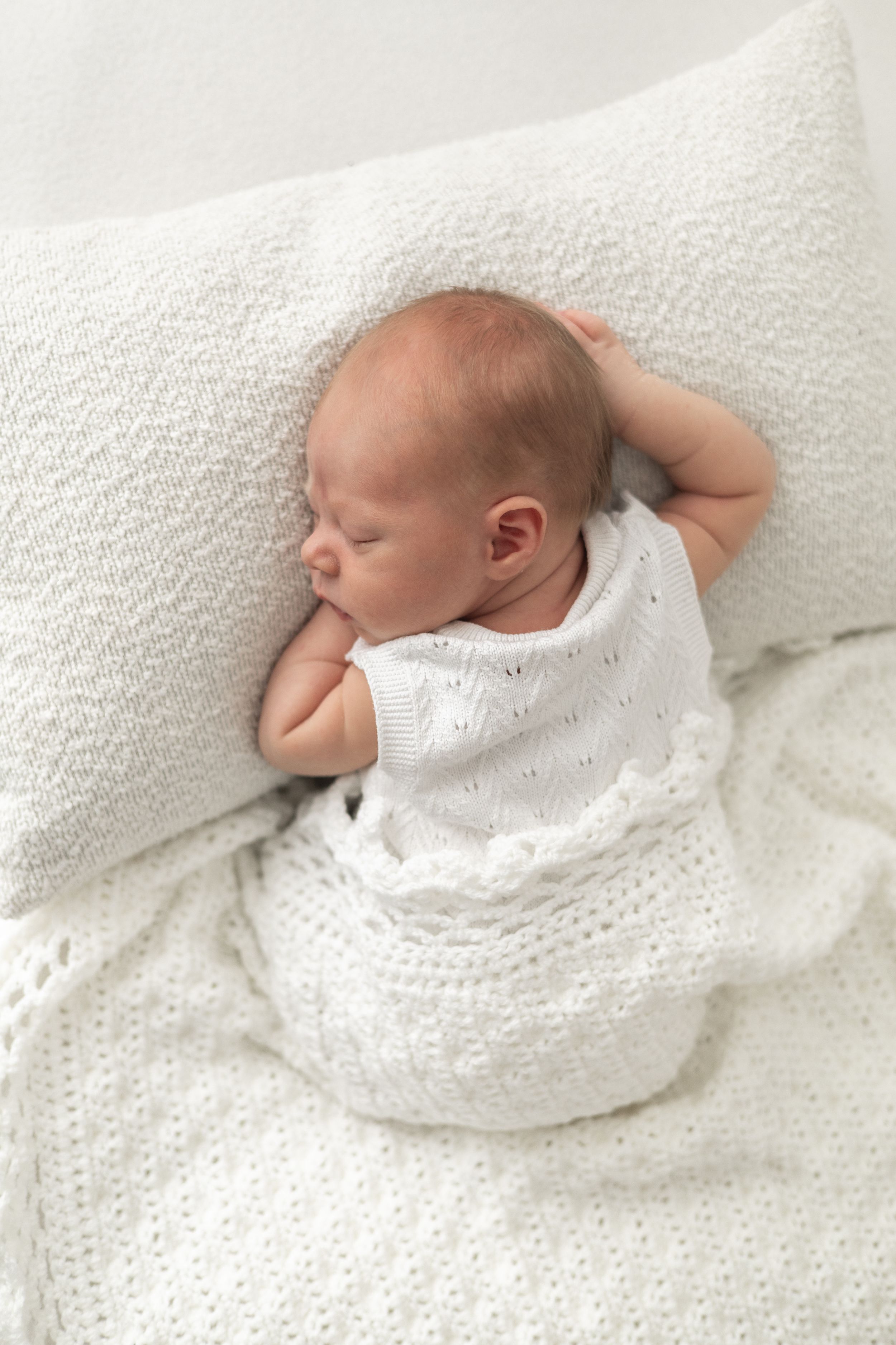 Peaceful newborn baby sleeping on white knit blanket and pillow, wrapped in white crochet swaddle natural newborn photography Nottingham