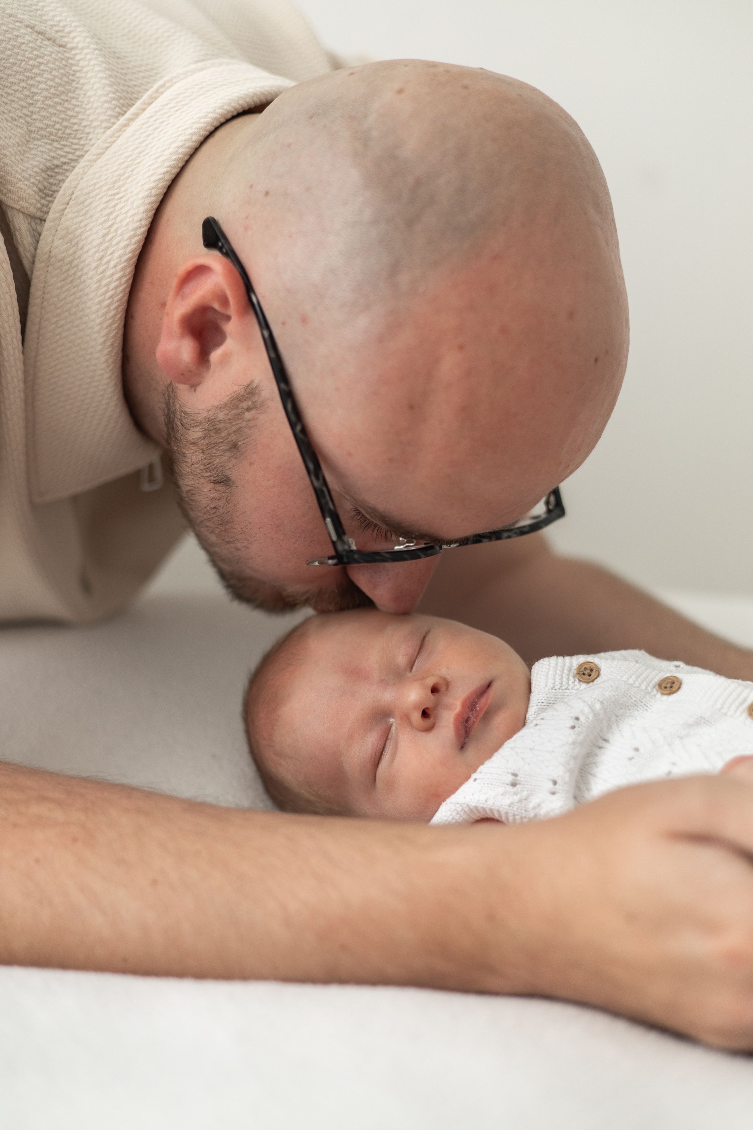 A Dad tenderly kisses sleeping newborn baby dressed in white onesie natural newborn photography Nottingham
