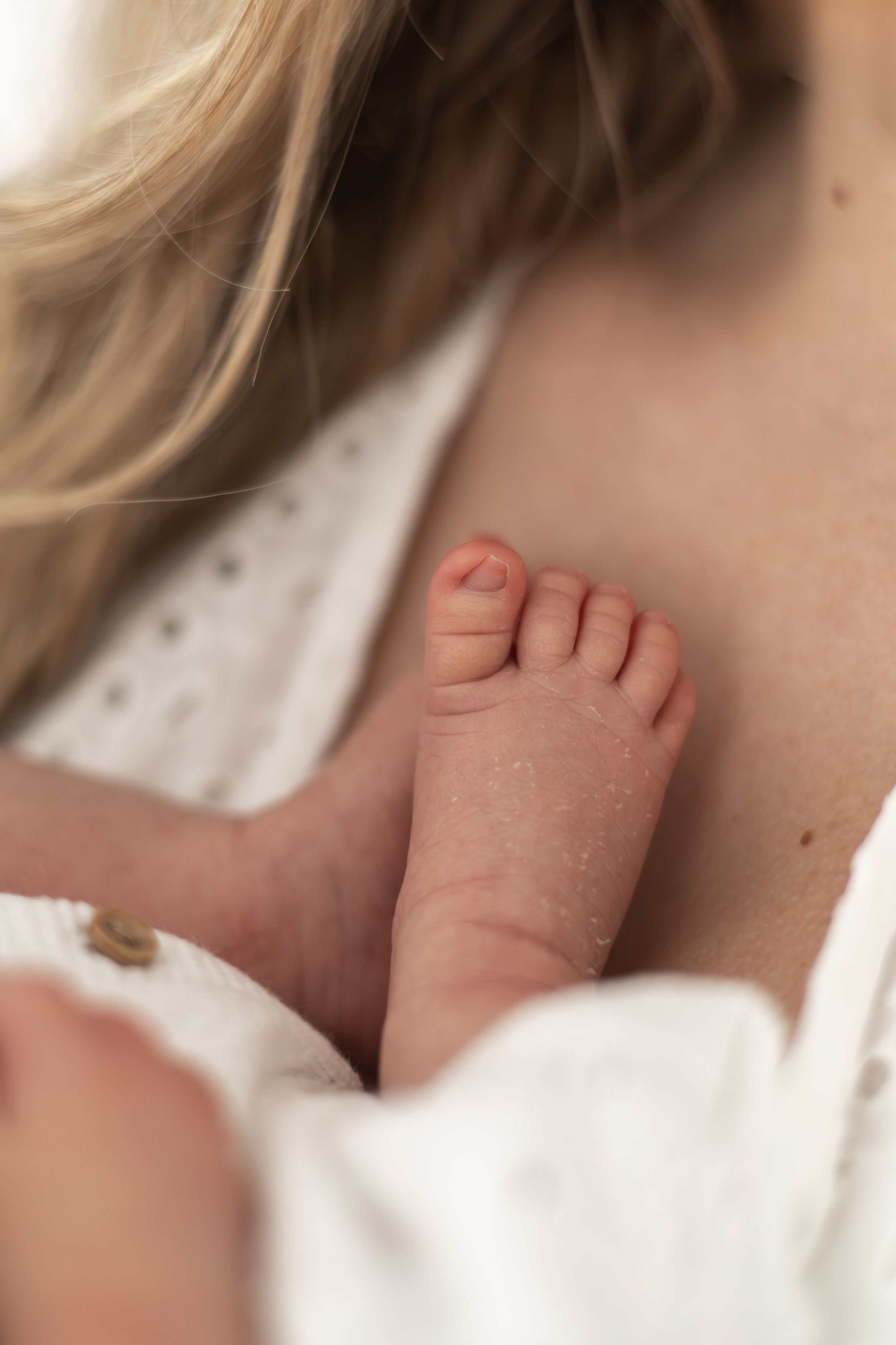 Close-up of a newborn baby's tiny foot resting against a mother's chest while being held natural newborn photography Nottingham