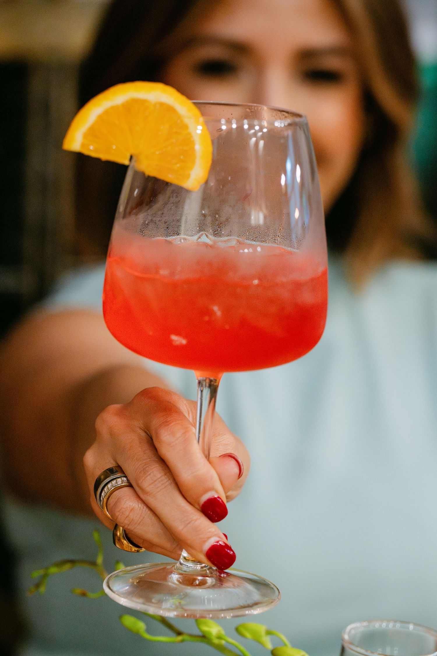 Woman holding a red cocktail in a wine glass garnished with an orange slice.