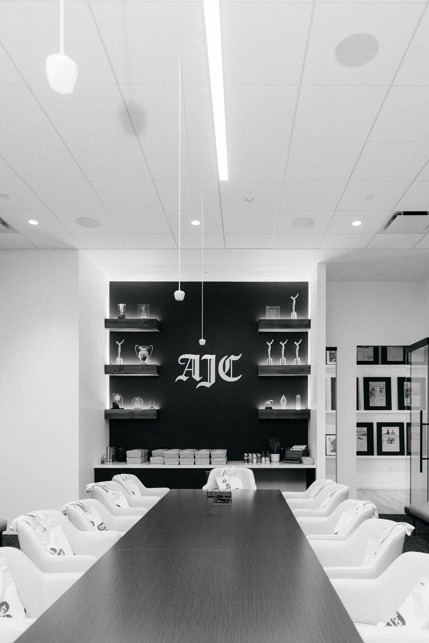 Black and white photo of a modern nail salon with white pedicure chairs, dark table, and AJC logo on feature wall.