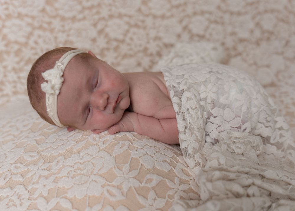 Peaceful newborn baby girl sleeping on a lace blanket wrapped in a white lace wrap.