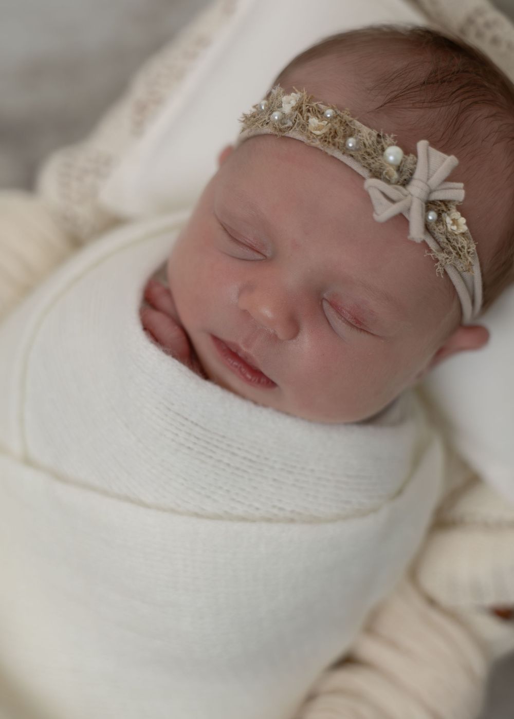Sleeping newborn baby wrapped in cream with a delicate pearl and bow headband.