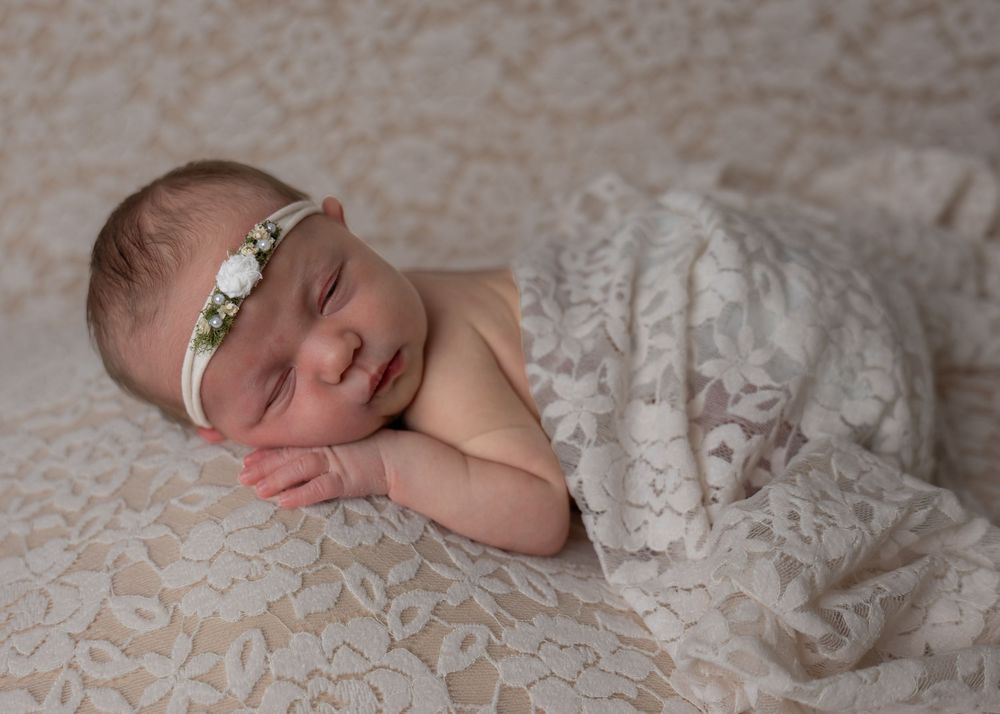 Newborn baby girl sleeping on a lace blanket with a delicate floral headband.