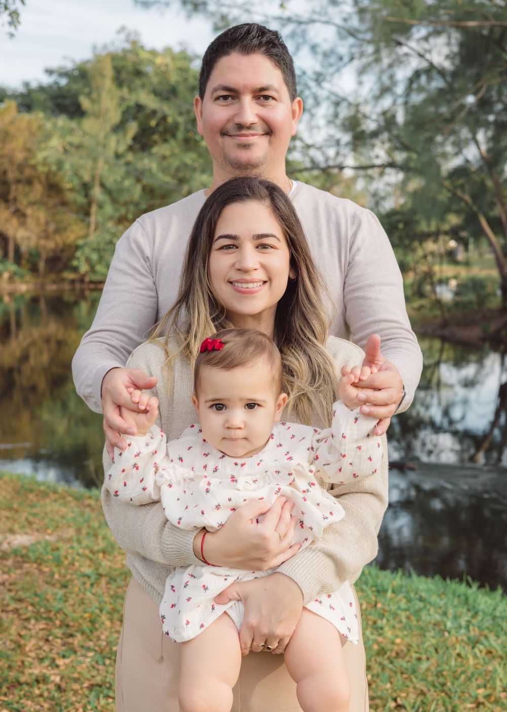 Outdoor family portrait taken near water with autumn foliage in background.
