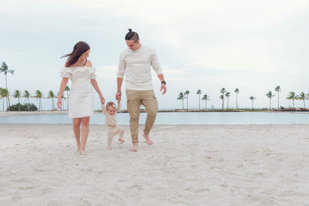 Family walks together holding hands on a tropical beach with palm trees and ocean in the background.