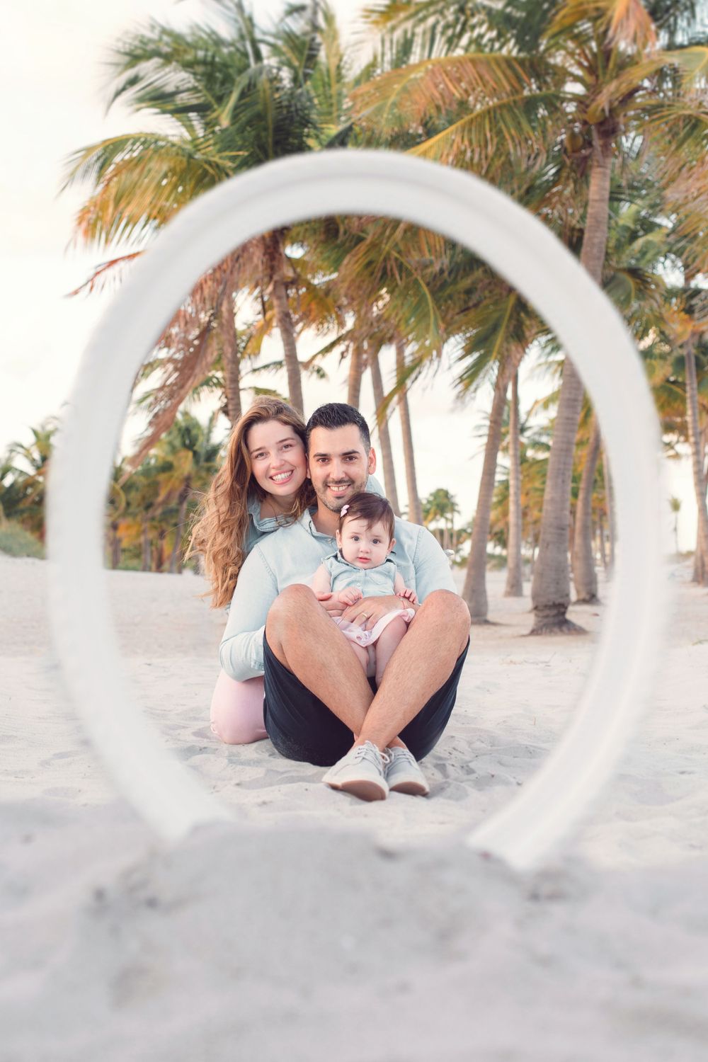 Creative beach portrait through white circular frame with palm trees in background.