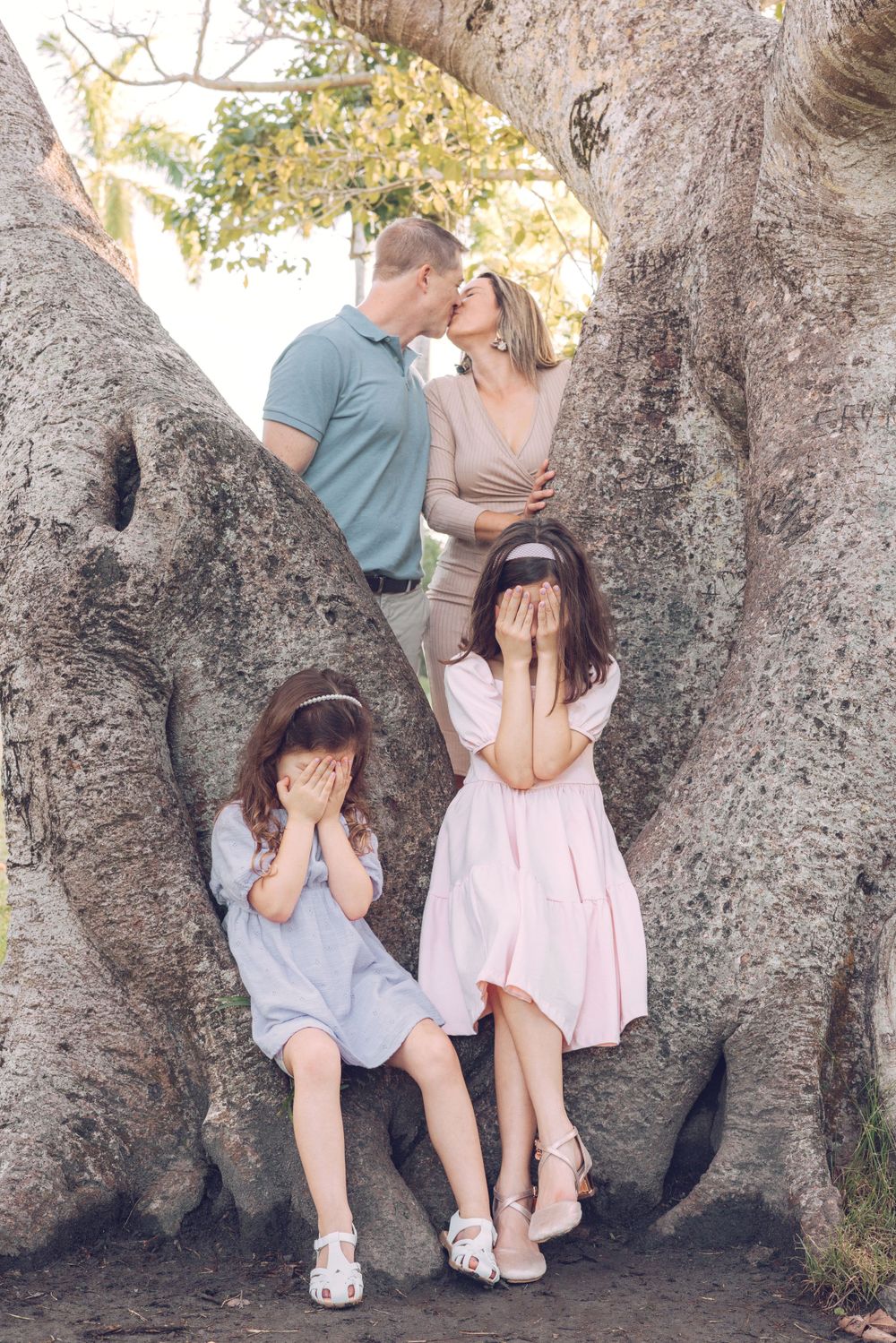 Playful family portrait in large tree trunk with children covering eyes.