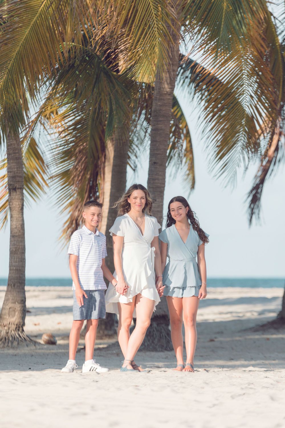 Family posing casually under palm trees on tropical beach.