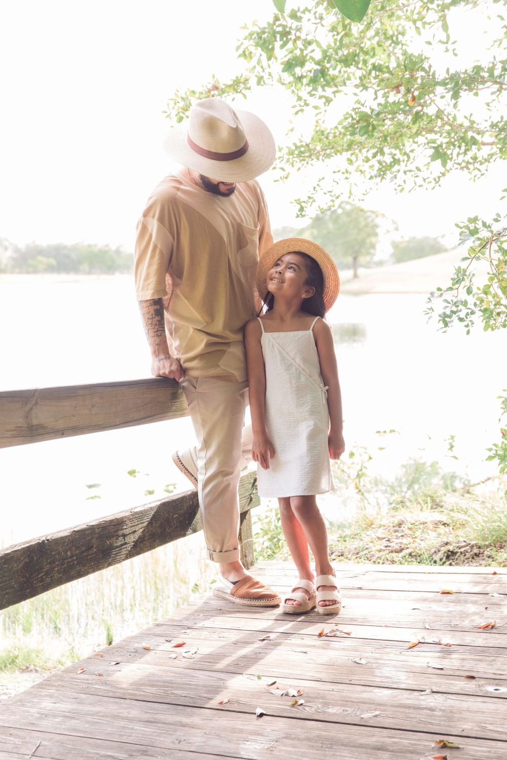 Parent and child sharing tender moment on wooden boardwalk wearing coordinated neutral outfits.