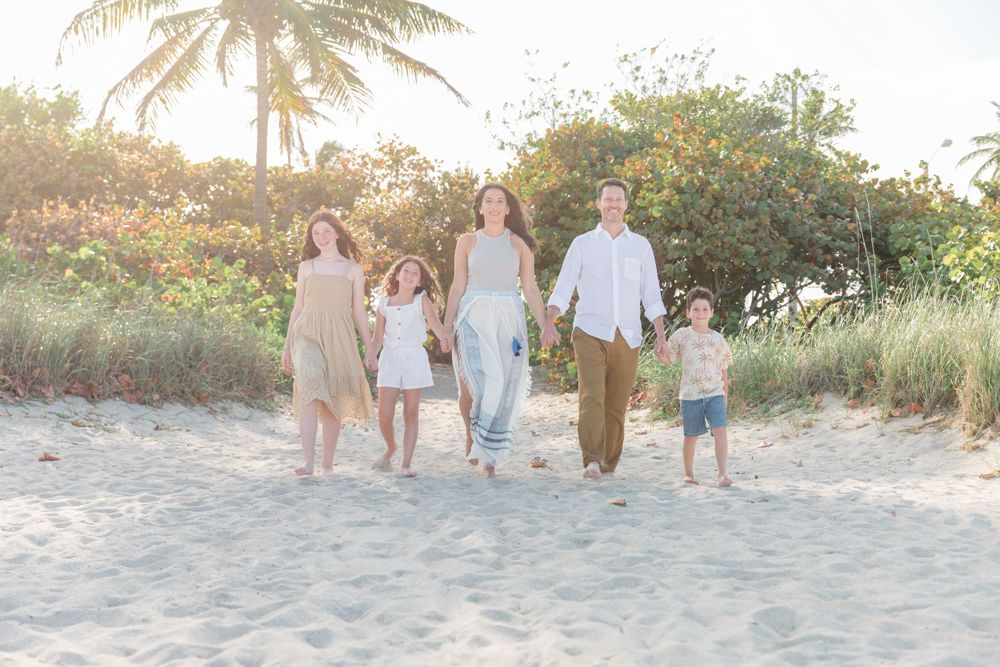 Candid beach photo capturing a family walking together on sandy path with palm trees at sunset.