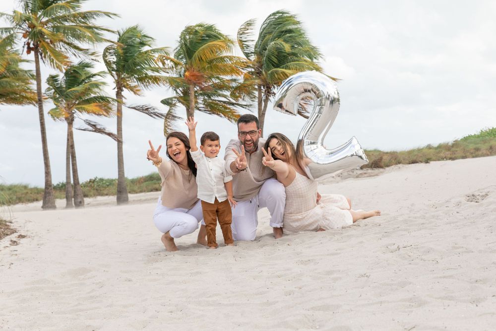 Beach celebration photo with silver number two balloon and palm trees swaying in wind.