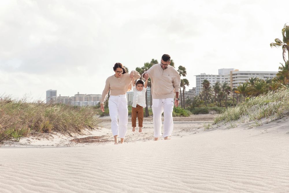 Family walking along scenic beach path with palm trees and buildings in background.