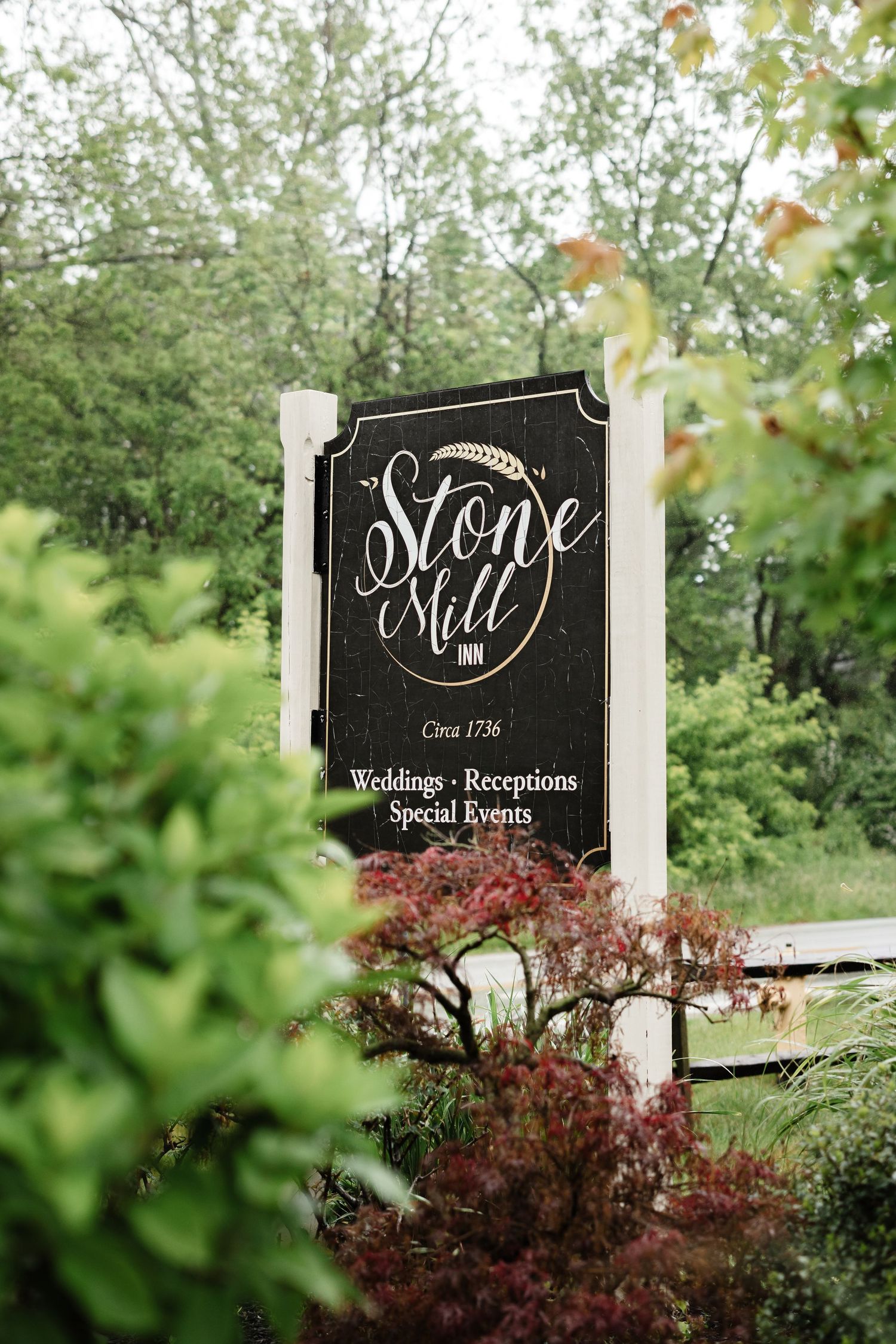 Stone Mill Inn sign circa 1736 advertising weddings, receptions, and special events among green trees.