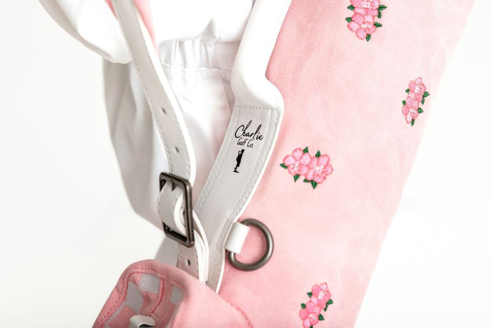 Pink floral golf bag with white leather strap and silver buckle detail, featuring elegant rose embroidery design.