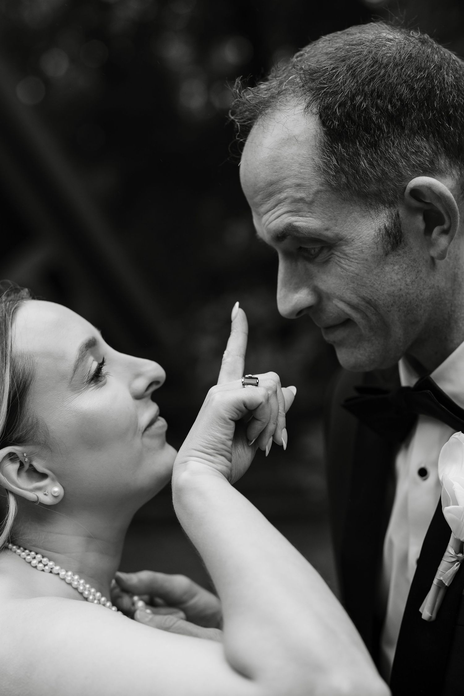 Black and white intimate portrait of bride touching grooms face tenderly at outdoor wedding.