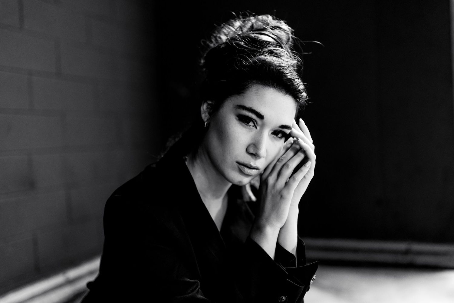 Ritratto in stile chiaroscuro in bianco e nero di una donna con i capelli raccolti, che tiene delicatamente le mani giunte vicino al mento.