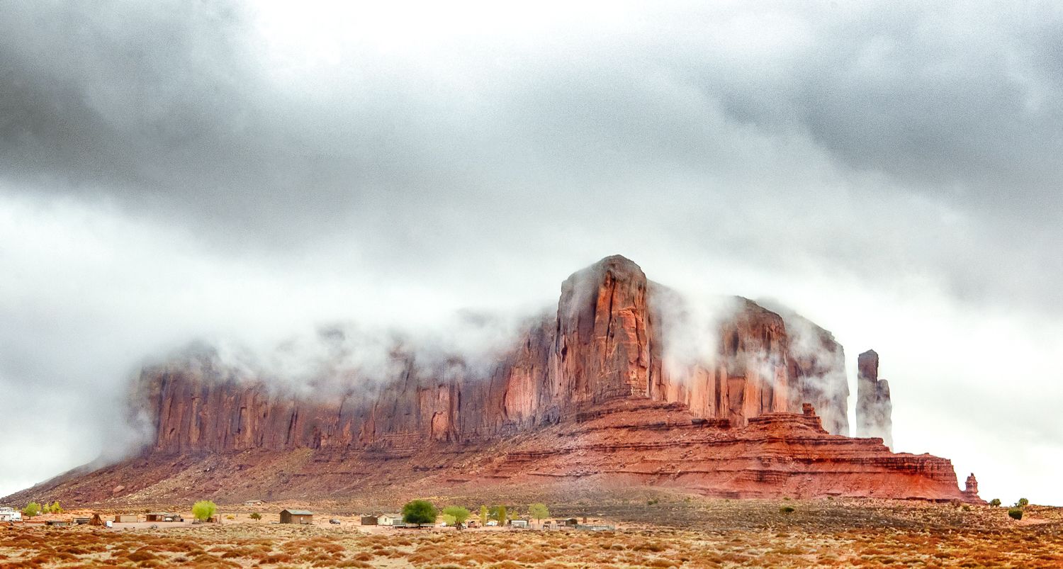 Red rock buttes of Monument Valley emerge through dramatic storm clouds and mist in the American Southwest desert.