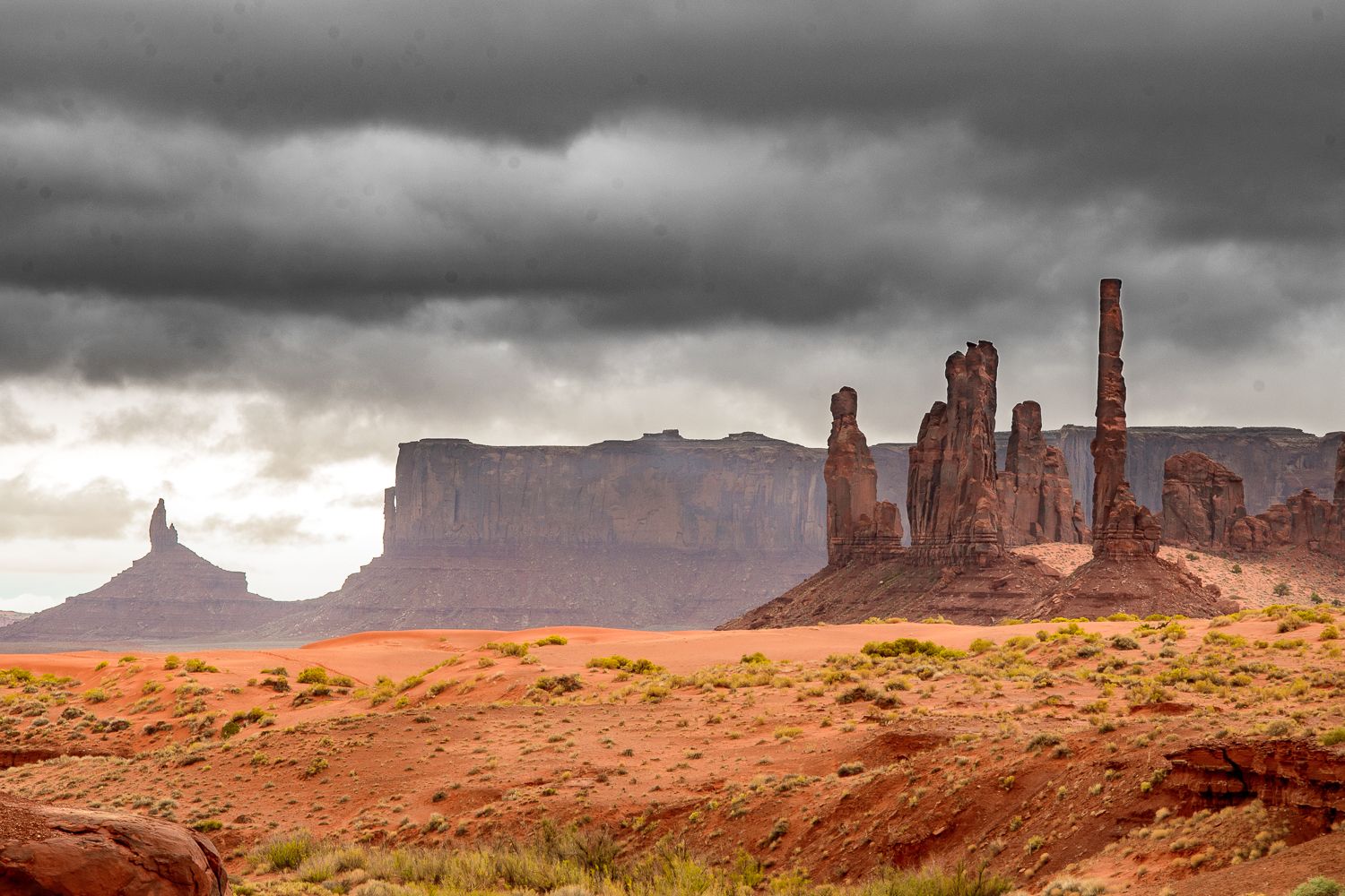 Dramatic storm clouds loom over Monument Valley's red sandstone buttes and spires in the Arizona desert.