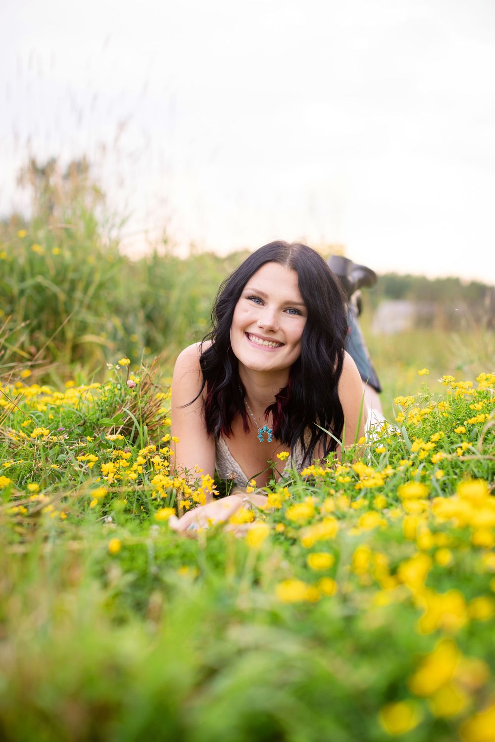 Smiling brunette woman lying in a field of yellow wildflowers, enjoying a sunny day outdoors in nature.