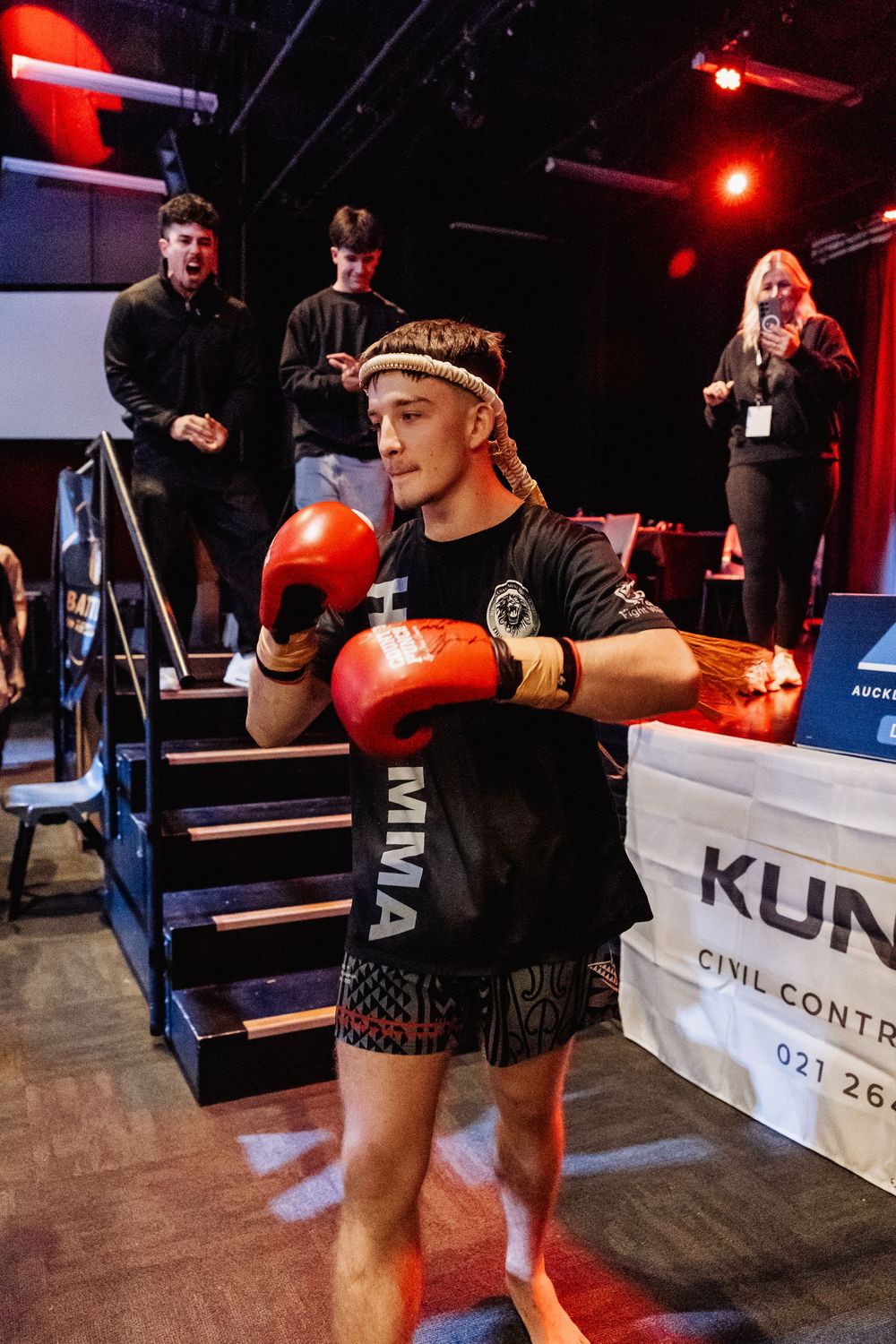 MMA fighter in red boxing gloves and tribal shorts poses in fighting stance at a martial arts event.