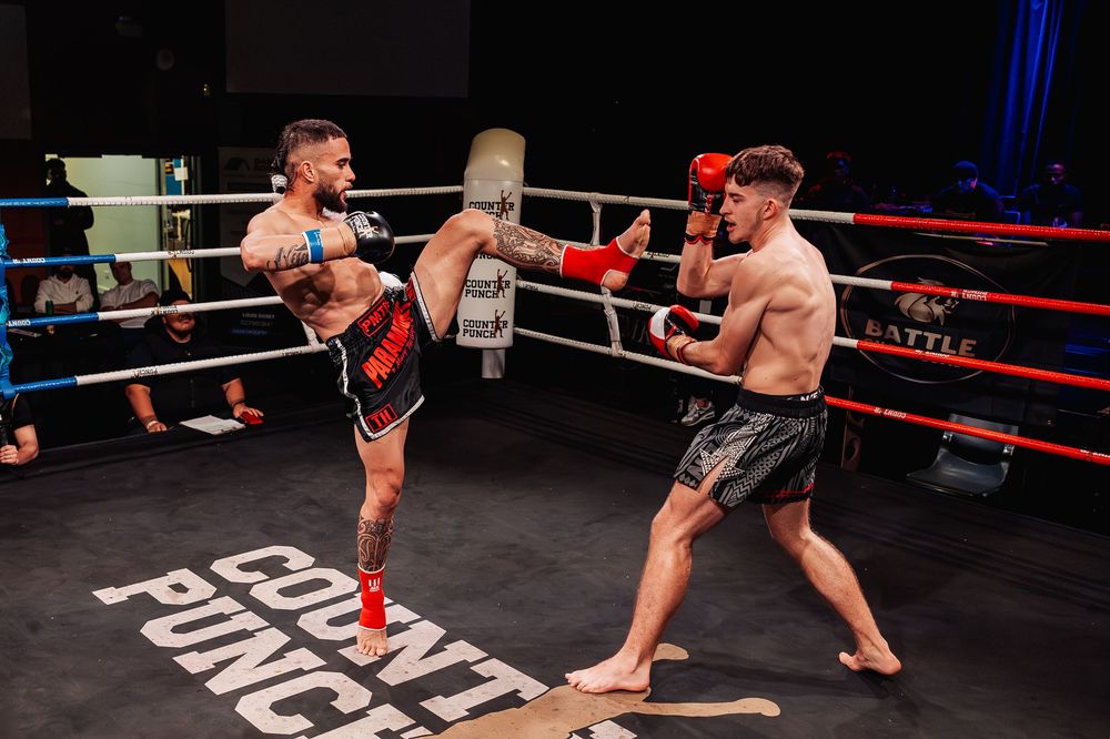 Two kickboxers sparring in a boxing ring during a competitive Muay Thai fight under bright event lights.