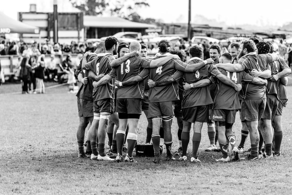 Rugby team huddles together on field in black and white photo.