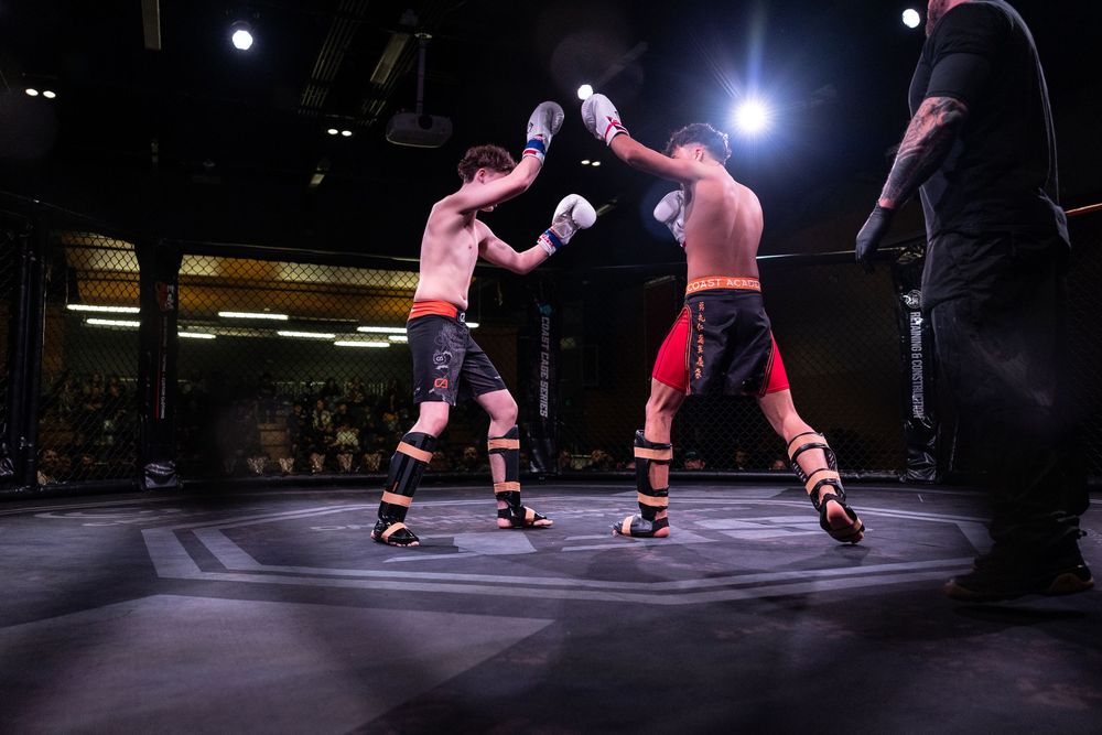 Two fighters exchange punches in a professional MMA bout under bright arena lights in an octagon cage.