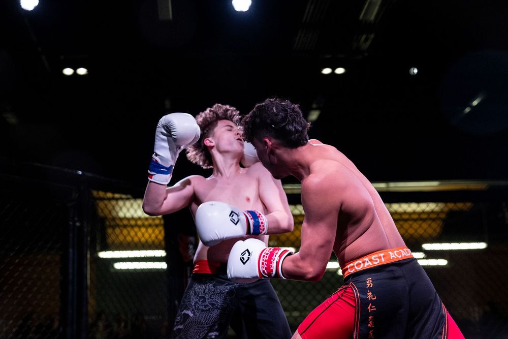 Two male boxers sparring in a ring, one wearing white gloves throwing a punch at his opponent.