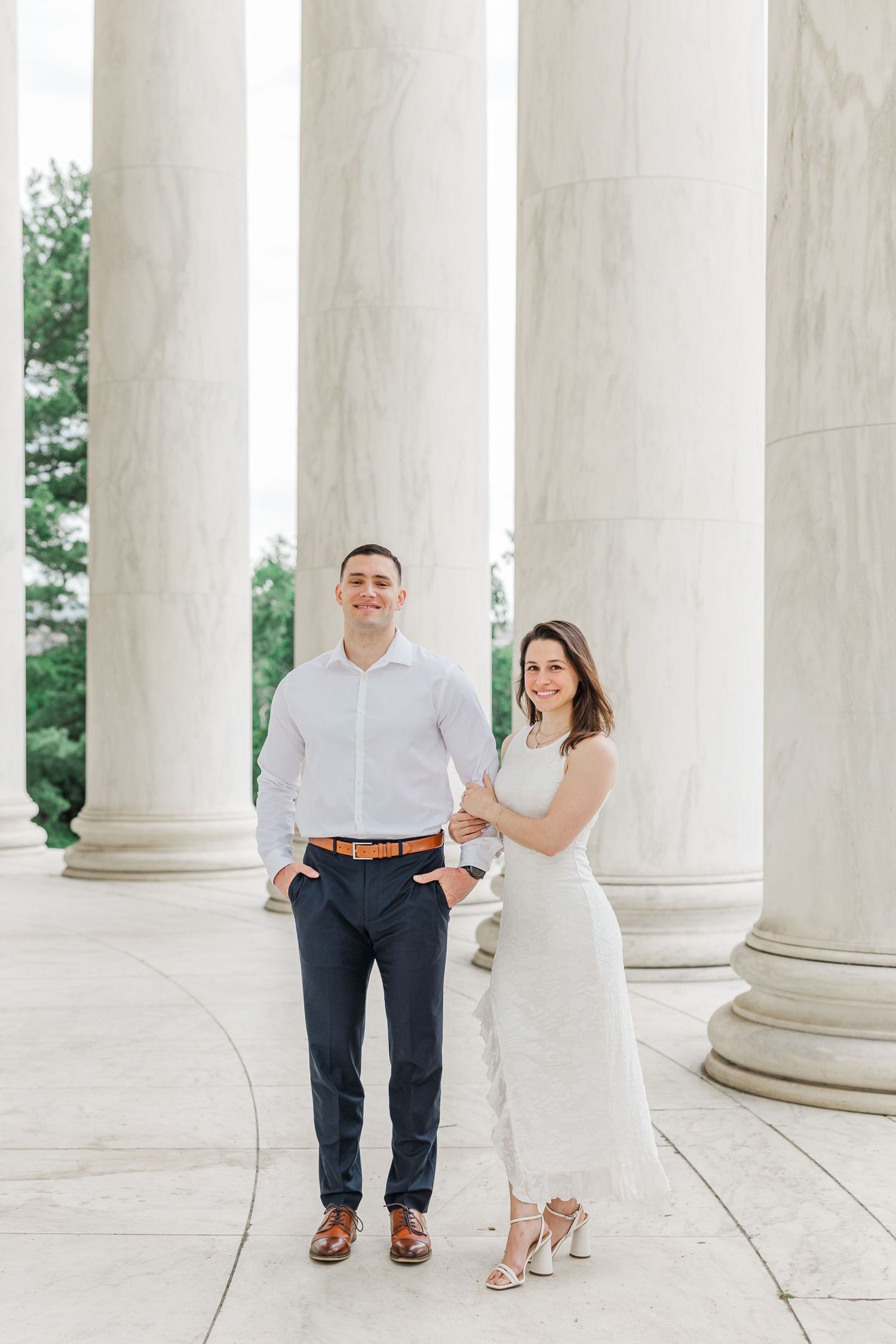 Couple posing at Jefferson Memorial columns, man in white shirt and navy pants, woman in white dress, Washington DC.
