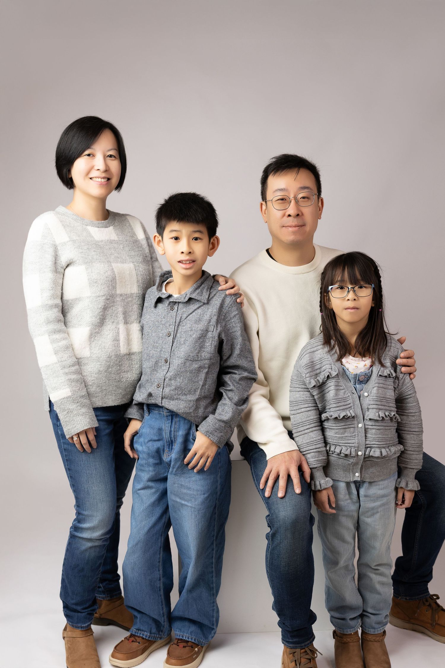 Asian family of four posing together in coordinating gray and blue outfits for a studio portrait photo.
